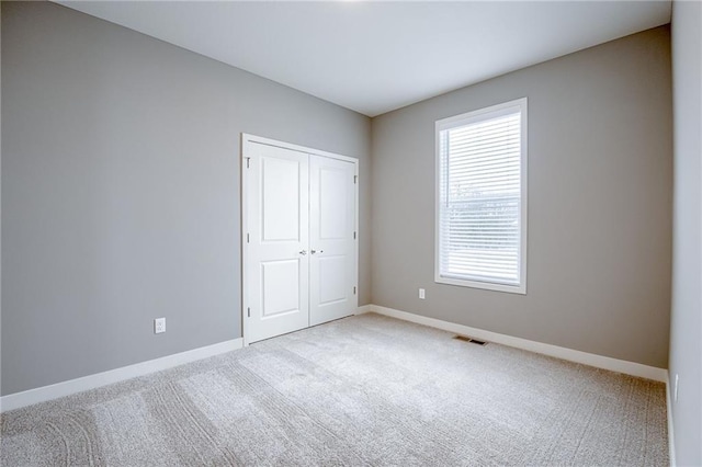 unfurnished bedroom featuring carpet, visible vents, a closet, and baseboards