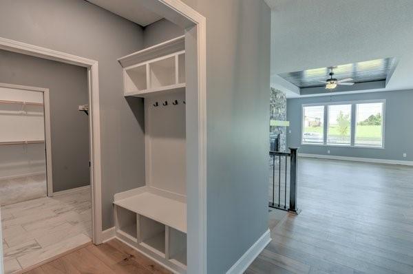 mudroom featuring wood finished floors, baseboards, a tray ceiling, a fireplace, and ceiling fan