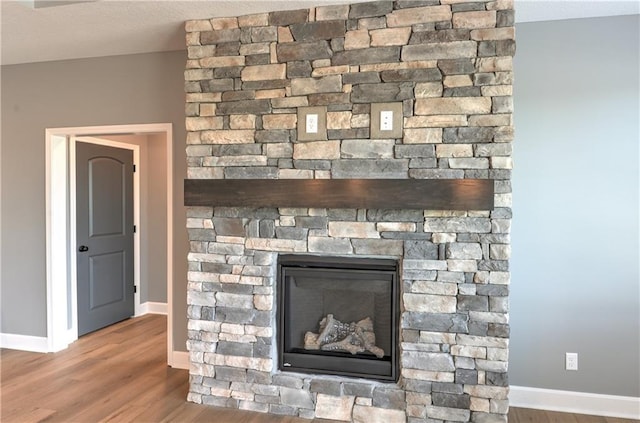 details featuring baseboards, a stone fireplace, and wood finished floors