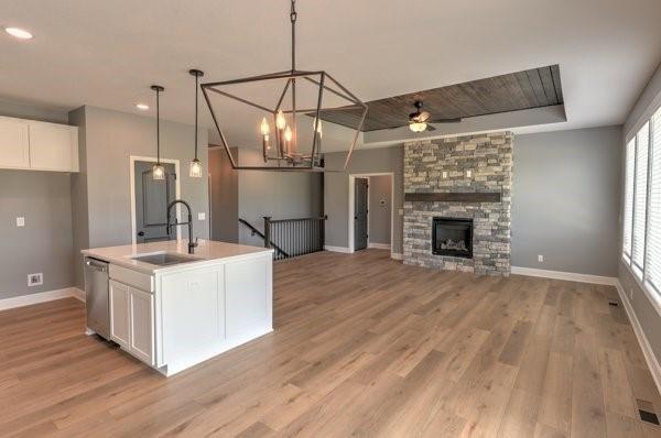 kitchen with light wood-style flooring, a sink, stainless steel dishwasher, white cabinetry, and a stone fireplace