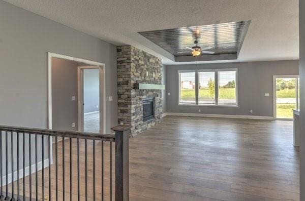 unfurnished living room featuring baseboards, a stone fireplace, wood finished floors, a textured ceiling, and a raised ceiling