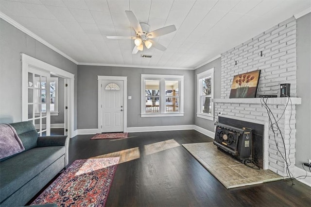 living room featuring dark wood-type flooring, a wood stove, ceiling fan, and crown molding