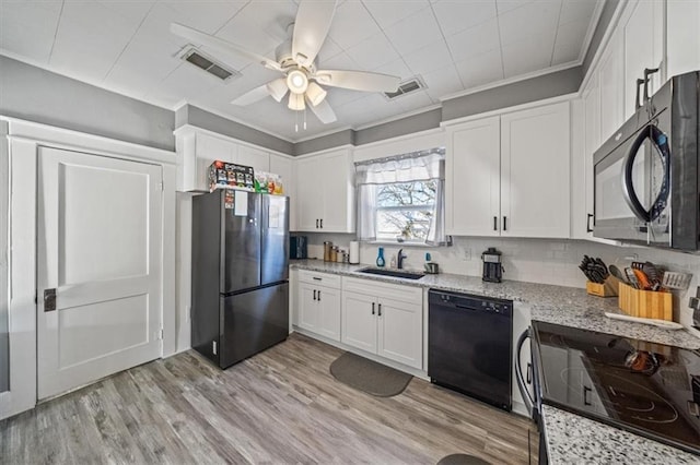 kitchen with light stone counters, sink, white cabinets, and black appliances