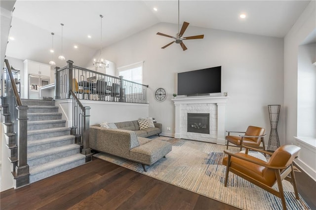 living room featuring a fireplace, high vaulted ceiling, dark wood-type flooring, and ceiling fan with notable chandelier