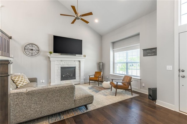 living room featuring dark hardwood / wood-style flooring, high vaulted ceiling, a stone fireplace, and ceiling fan