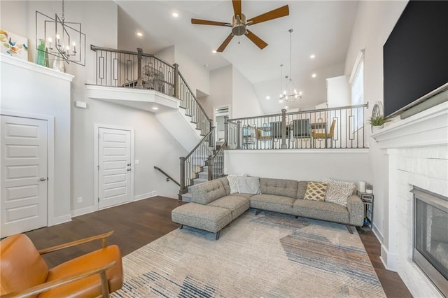 living room with ceiling fan, dark hardwood / wood-style floors, a towering ceiling, and a tile fireplace