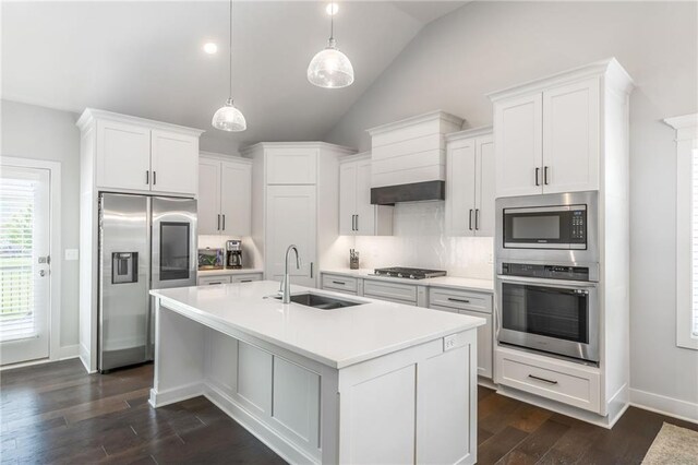 kitchen with sink, stainless steel appliances, pendant lighting, lofted ceiling, and a kitchen island with sink