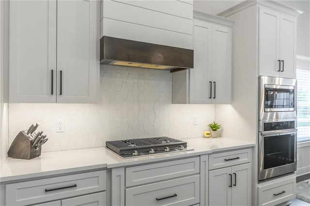 kitchen with backsplash, white cabinets, wall chimney range hood, and appliances with stainless steel finishes