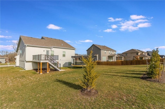 rear view of property with a lawn, a trampoline, and a deck