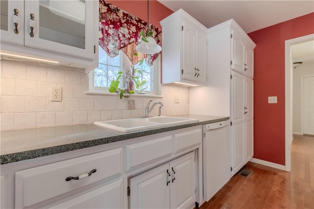 kitchen featuring tasteful backsplash, dishwasher, sink, light wood-type flooring, and white cabinets