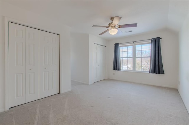 unfurnished bedroom with ceiling fan, light colored carpet, lofted ceiling, and multiple closets