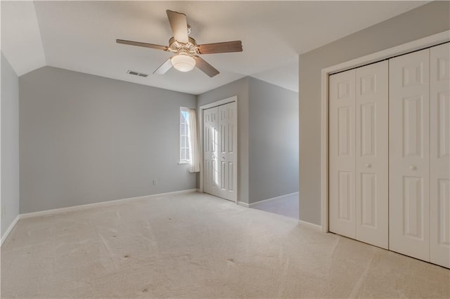 unfurnished bedroom with ceiling fan, light carpet, vaulted ceiling, and multiple closets