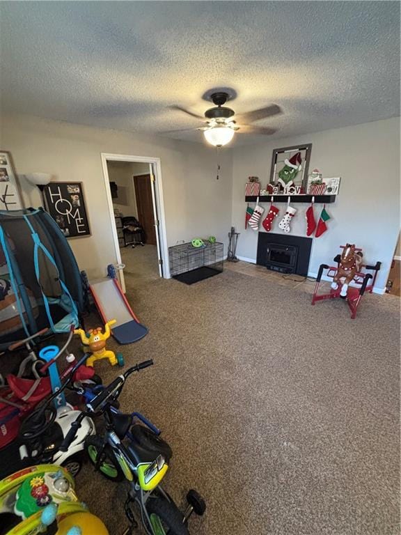 recreation room featuring ceiling fan, a fireplace, carpet floors, and a textured ceiling