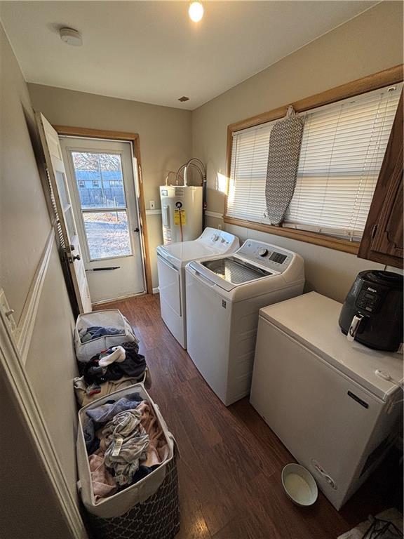 laundry area featuring washing machine and clothes dryer, water heater, dark hardwood / wood-style flooring, and cabinets