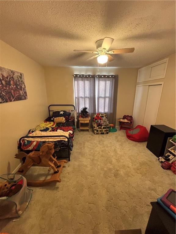 bedroom with carpet flooring, ceiling fan, a closet, and a textured ceiling