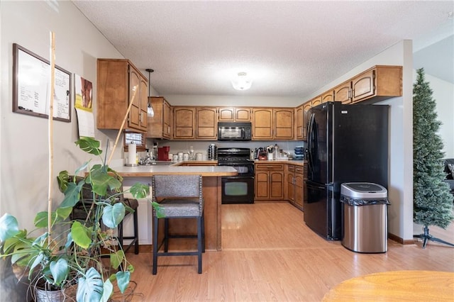 kitchen with black appliances, a breakfast bar, light wood-type flooring, and kitchen peninsula