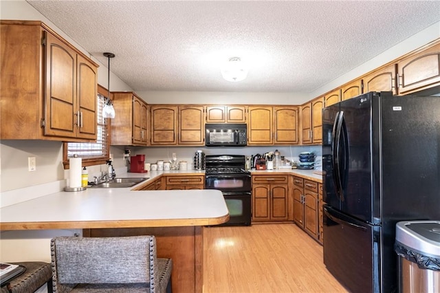 kitchen with kitchen peninsula, a kitchen breakfast bar, sink, black appliances, and light hardwood / wood-style flooring