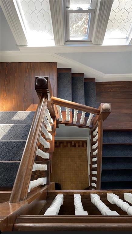 stairs with a wealth of natural light, crown molding, and wood walls