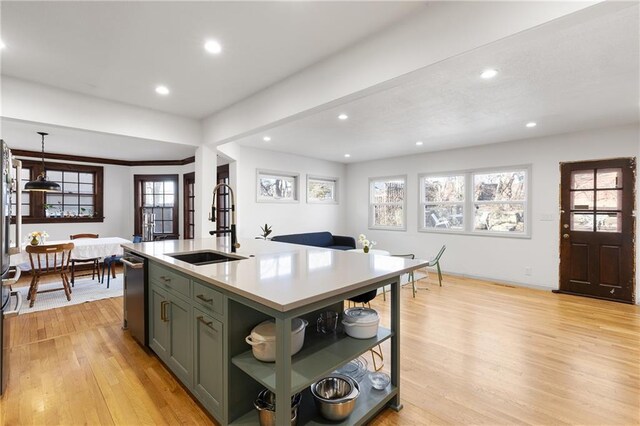 kitchen with an island with sink, dishwasher, sink, green cabinetry, and light hardwood / wood-style flooring