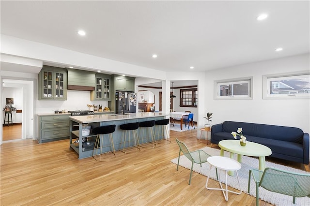 kitchen featuring wall chimney range hood, light hardwood / wood-style flooring, stainless steel refrigerator, a breakfast bar, and green cabinetry