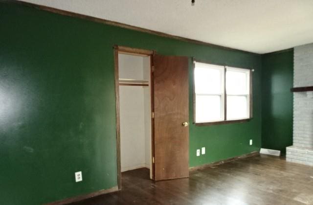 unfurnished bedroom with a brick fireplace, a closet, and dark wood-type flooring