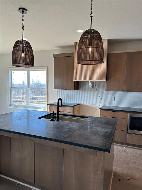 kitchen with decorative backsplash, pendant lighting, a kitchen island with sink, and sink