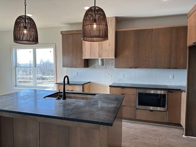 kitchen featuring stainless steel microwave, tasteful backsplash, hanging light fixtures, and sink