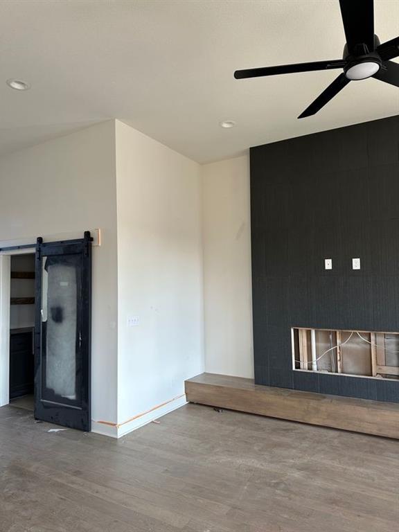 unfurnished room with ceiling fan, a barn door, and wood-type flooring