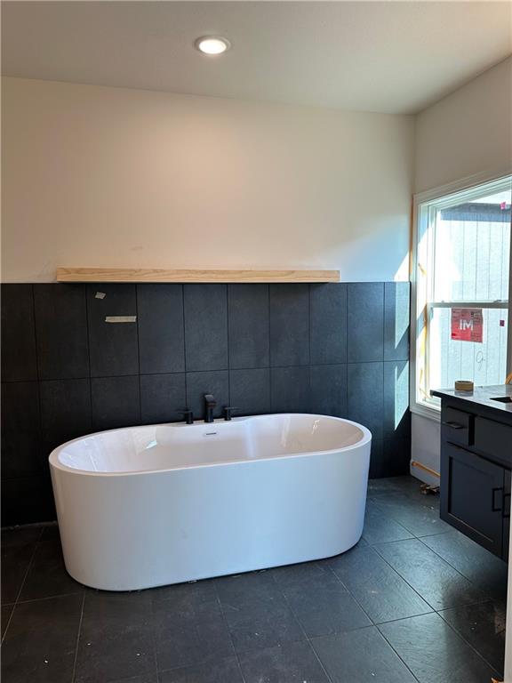 bathroom featuring tile patterned floors, vanity, a tub to relax in, and tile walls