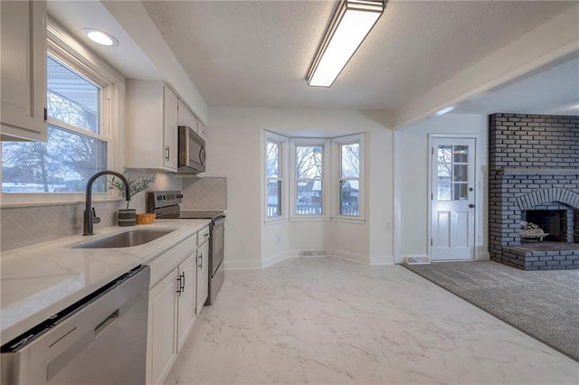 kitchen featuring sink, a brick fireplace, tasteful backsplash, white cabinetry, and stainless steel appliances