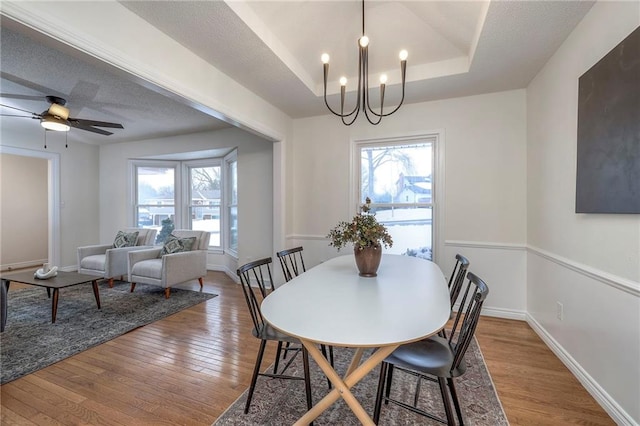 dining space featuring a raised ceiling, a healthy amount of sunlight, ceiling fan with notable chandelier, and hardwood / wood-style flooring