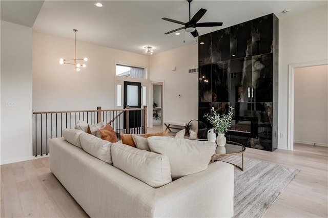 living room featuring ceiling fan with notable chandelier, a high ceiling, light wood-type flooring, and a premium fireplace