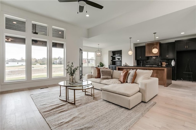 living room with ceiling fan with notable chandelier, sink, and light hardwood / wood-style flooring