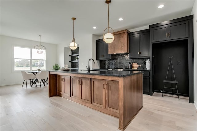 kitchen with sink, an island with sink, pendant lighting, decorative backsplash, and light wood-type flooring