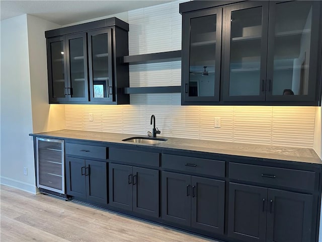 kitchen with tasteful backsplash, wine cooler, glass insert cabinets, light wood-style floors, and a sink