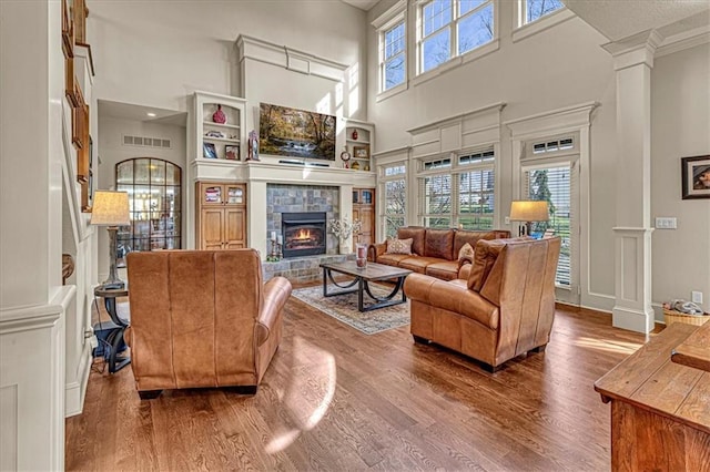 living room with ornate columns, a towering ceiling, a tile fireplace, and hardwood / wood-style flooring