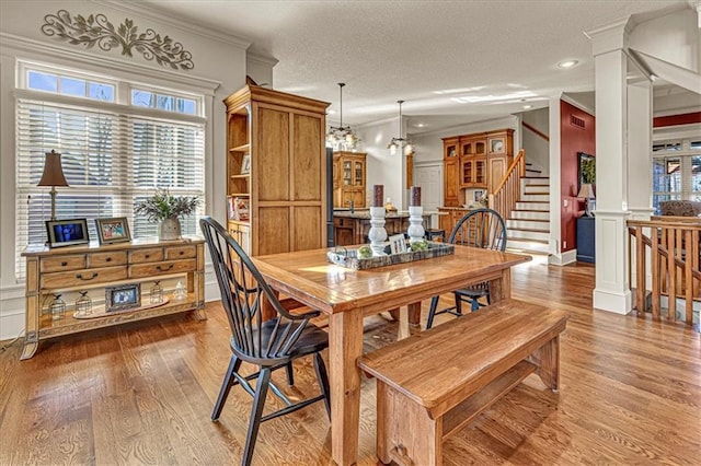 dining room featuring a textured ceiling, light hardwood / wood-style flooring, crown molding, and decorative columns