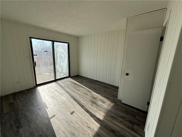 spare room featuring dark wood-type flooring, wooden walls, and a textured ceiling