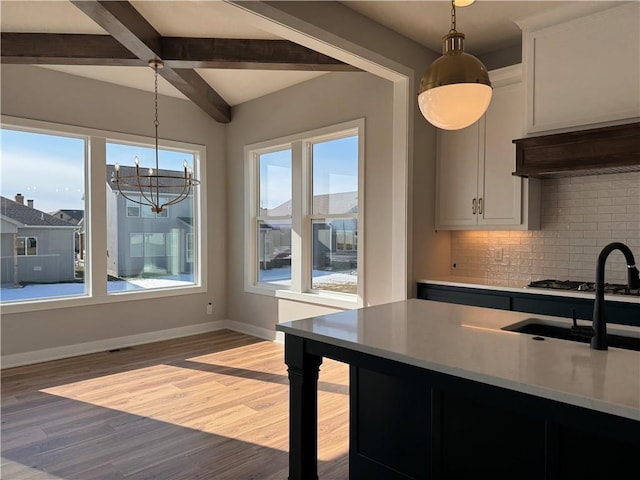 kitchen with hanging light fixtures, beam ceiling, light hardwood / wood-style floors, decorative backsplash, and white cabinets