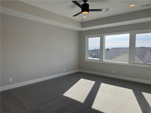 unfurnished room with a raised ceiling, ceiling fan, and dark carpet