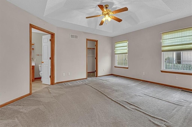 unfurnished room featuring a raised ceiling, ceiling fan, light colored carpet, and a textured ceiling