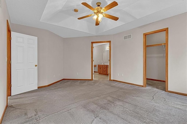 unfurnished bedroom with ensuite bath, ceiling fan, a spacious closet, a textured ceiling, and light carpet