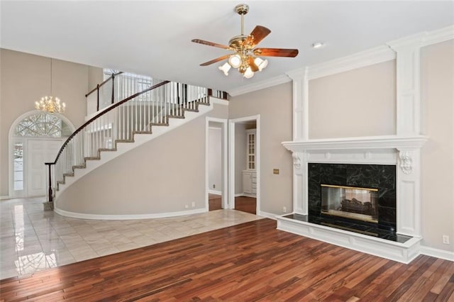 unfurnished living room with a premium fireplace, ceiling fan with notable chandelier, crown molding, and wood-type flooring