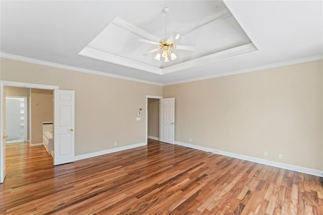 empty room with a tray ceiling, ornamental molding, hardwood / wood-style floors, and ceiling fan