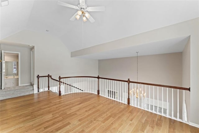 spare room featuring ceiling fan with notable chandelier, vaulted ceiling, and wood-type flooring