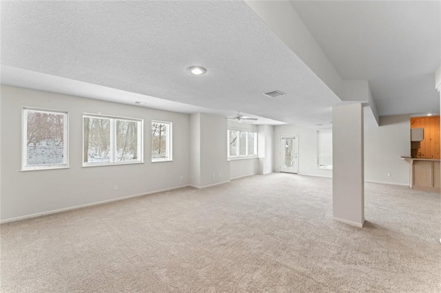 basement with a textured ceiling, ceiling fan, and light colored carpet