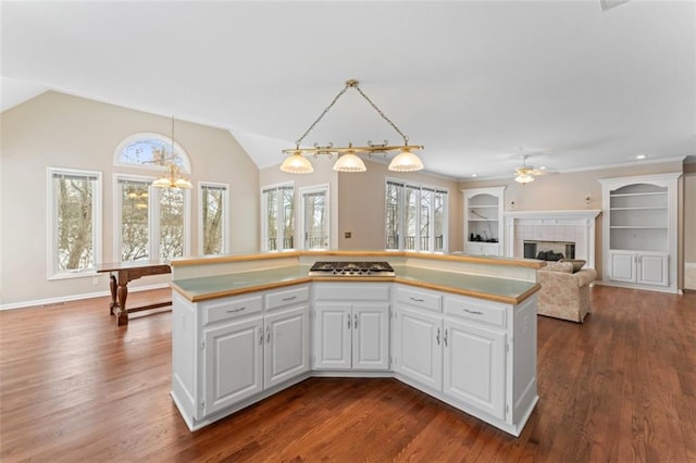 kitchen featuring dark wood-type flooring, a tiled fireplace, decorative light fixtures, a center island, and white cabinetry