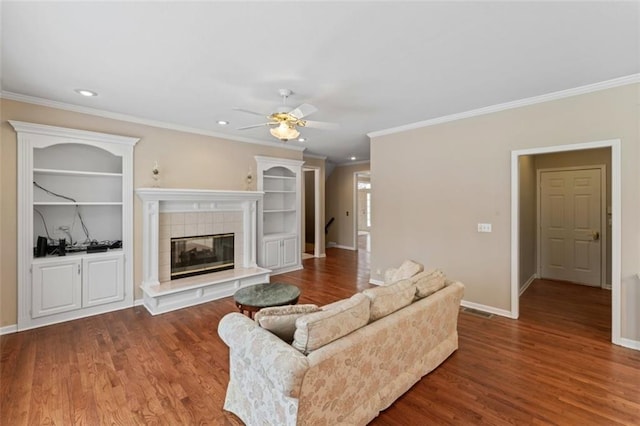 living room with a tile fireplace, crown molding, ceiling fan, and wood-type flooring