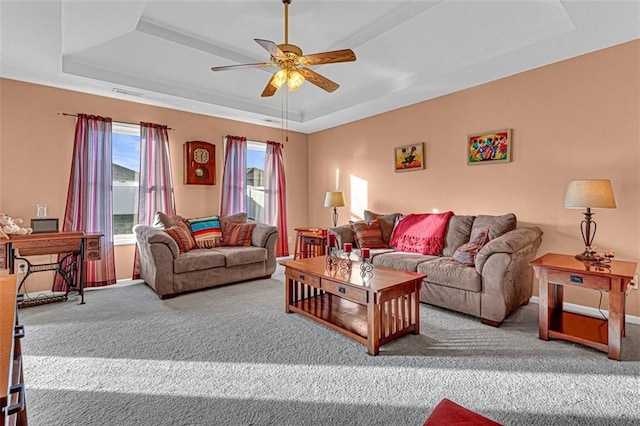 living room featuring a raised ceiling, ceiling fan, and carpet