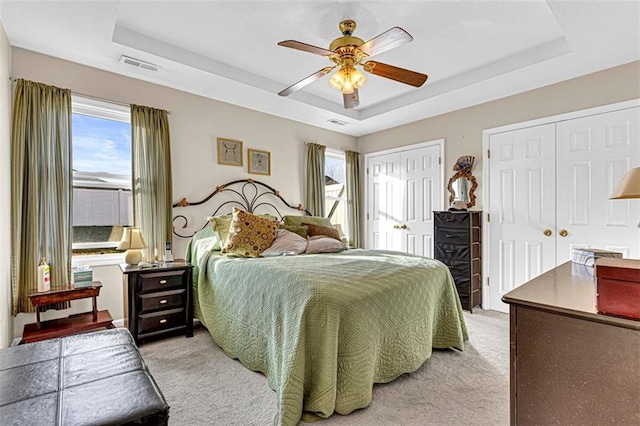 carpeted bedroom featuring a tray ceiling, multiple windows, and ceiling fan